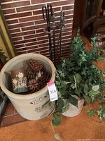 Metal fireplace tools in black with stand positioned behind large ceramic planter and faux plant.