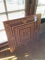 Full view of folded wooden table with intricate geometric inlay pattern leaning against window blinds, showing design and size.