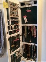 Open white wooden jewelry armoire showing interior, green felt lining with hanging necklaces and earrings