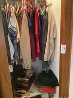 Photo showing men's jackets and shirts hanging on hangers in a closet, in various colors including beige, blue, and red.