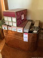 Photo showing copper metal bucket with multiple boxes of music rolls placed on and inside the bucket