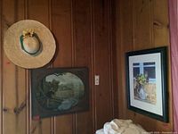 Wide shot showing both art pieces and the straw hat hanging on wood panel wall