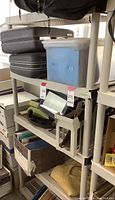 Plastic shelving unit with 4 grid shelves and beige legs. Top shelf holds a blue storage container and other items.