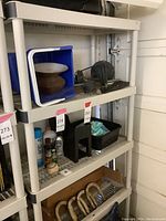 Shelving unit filled with various items including a blue bin with household goods, black plastic trays, wooden hooks, and assorted bottles.