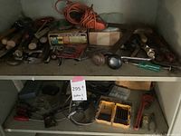 Overview of a shelf containing various hand tools such as hammers, wrenches, screwdrivers, ladles, and drill bit sets.
