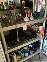 Shelving unit with assorted handtools, glass jars, cleaning sprays, and gardening supplies.