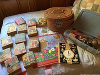 Overview of vintage children's books laid out on bed with sewing basket and plastic organizer box visible to the right