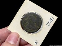 Front side of 1802 Draped Bust penny showing profile of Draped Bust design and year handwritten on holder.