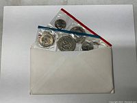 Coins in original sealed mint packaging partially visible in an envelope, showing uncirculated condition and packaging details indicating Philadelphia and Denver mint sets.