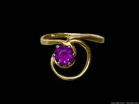 Close-up image of gold ring with round purple stone on black background showing detailed swirl design and prong setting.