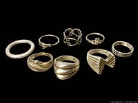Eight sterling silver rings arranged in two rows on black background, showing variety of designs and thicknesses.