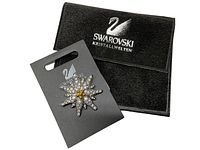 Swarovski rhinestone starburst brooch displayed on black Swarovski card alongside black velvet Swarovski Kristallwelten pouch.