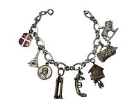 Image of sterling silver charm bracelet with various distinct charms including a red shield, Eiffel Tower, portrait medallion, binoculars, firearm, cuckoo clock, barrel, and lion figure.