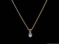 Close-up front view of necklace pendant showing oval tanzanite gemstone and small diamond on 14K chain against black background.