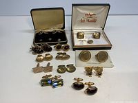 Overview of the collection showing multiple pairs of cufflinks in two original boxes and loose on table surface
