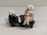 Side view of ceramic vintage singing cats shakers showing one cat at piano in black suit and one cat singing in pink dress, sitting on piano bench.