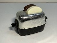 Front view of the silver-speckled vintage toaster base with cream-colored toast-shaped shaker on top, showing mechanical push-up detail.