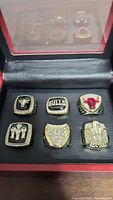 Six Michael Jordan Chicago Bulls replica championship rings displayed in a protective black and wooden case with glass cover. Close-up showing ring designs and condition.