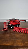 Side view of CASE 1/32 Axial-Flow combine model with one detachable header attachment placed in front and another header attachment beside it.