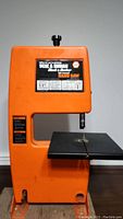 Full view of the orange Black & Decker band saw with metal cutting table and blade on the front.