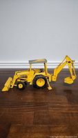 Side view of yellow John Deere loader backhoe scale diecast model showing full length with loader and backhoe arms extended.