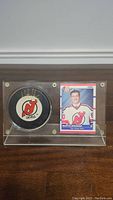 Clear frontal view of display case containing autographed puck and rookie card together.