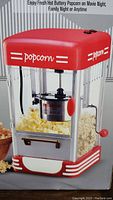Red and white Bridgeland tabletop popcorn machine with clear sides and visible stirring mechanism with red handle.
