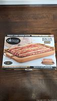 Box front showing the Gotham Copper Bacon Pan with bacon on the rack and text about cooking 12 slices and non-stick coating.