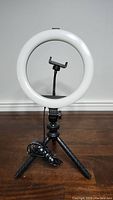 Full view of white circular USB ring light mounted on adjustable black tripod with phone holder in the ring center.