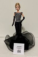 Front view of Barbie doll wearing black and silver evening gown with flared tulle train, standing upright.