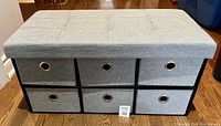 Front view of gray storage bench showing six fabric drawers in different gray tones and tufted upholstered seat