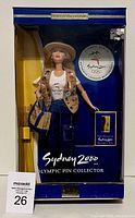 Front view of the Barbie doll in original packaging showing clothing, pins, and tote bag with Sydney 2000 Olympics branding.