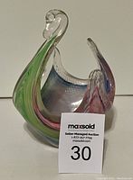 Front angle showing the swan with green and pink swirl accents, clear glass neck and detailed head.