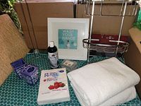 Photo showing mix of bathroom items including towels, soap, soap dish, hand soap, wall sign, and metal shower caddy.