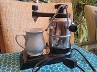 Photo of the cappuccino machine next to the ceramic Denby mug showing the lever, spout, and the base with power cord.