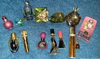 Top-down view of 14 assorted celebrity perfume bottles laid out on a blue carpet showing variety in bottle design and size.