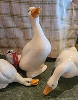 Photo showing all three ceramic birds with a Coke can for size reference. Birds have white glaze with orange beaks, poses vary. Small chip visible on lower bill of smallest bird.