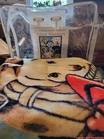 Photo of the folded blanket showing part of the puppy design with visible fabric texture and clear packaging in the background