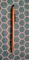 Full length photo of gold color Cross ballpoint pen on a blue geometric pattern background.
