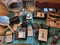 Full view of the lot, showing various electronic devices including calculators, camera, white handheld device, and other miscellaneous electronics on a blue patterned surface