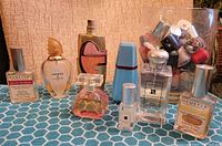 Front view of the lot showing eight fragrance bottles arranged on a blue patterned surface and a vase of assorted nail polishes in the background.
