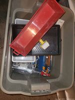 Top view of large plastic tote containing red plastic tray, small yellow hammer, various small boxes, and other assorted garage items.
