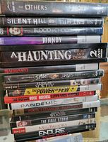 Side view of stacked DVD cases showing titles and covers of multiple horror and thriller movies.