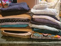 Stacked clothing items in neutral, black, white, pastel, and bright colors, folded and laid on a flat surface.