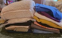Stack of folded ladies clothing items including fleece jacket, various tops and sweaters in multiple colors