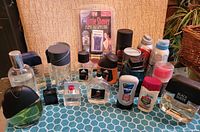 Wide view of all toiletry items on table showing new travel razor in packaging, multiple fragrance bottles including green and black bottle, various deodorants, and Black Suede cologne