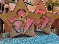 Two gold star-shaped gift boxes containing Pink Prosecco Rose beauty products arranged on a blue patterned surface.
