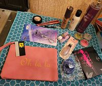 Photo showing full lot arranged on blue surface including cosmetic bag, eyelash curler, lip balms, lipsticks, mascara, brushes, compact, scrunchies, and fragrance mist