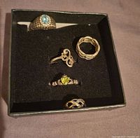 Full view of five rings displayed in black box showing variety of designs and stones.