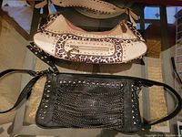 Two purses side by side on a glass table: leopard print purse with beige trimming and a black purse with stud and chain detailing.